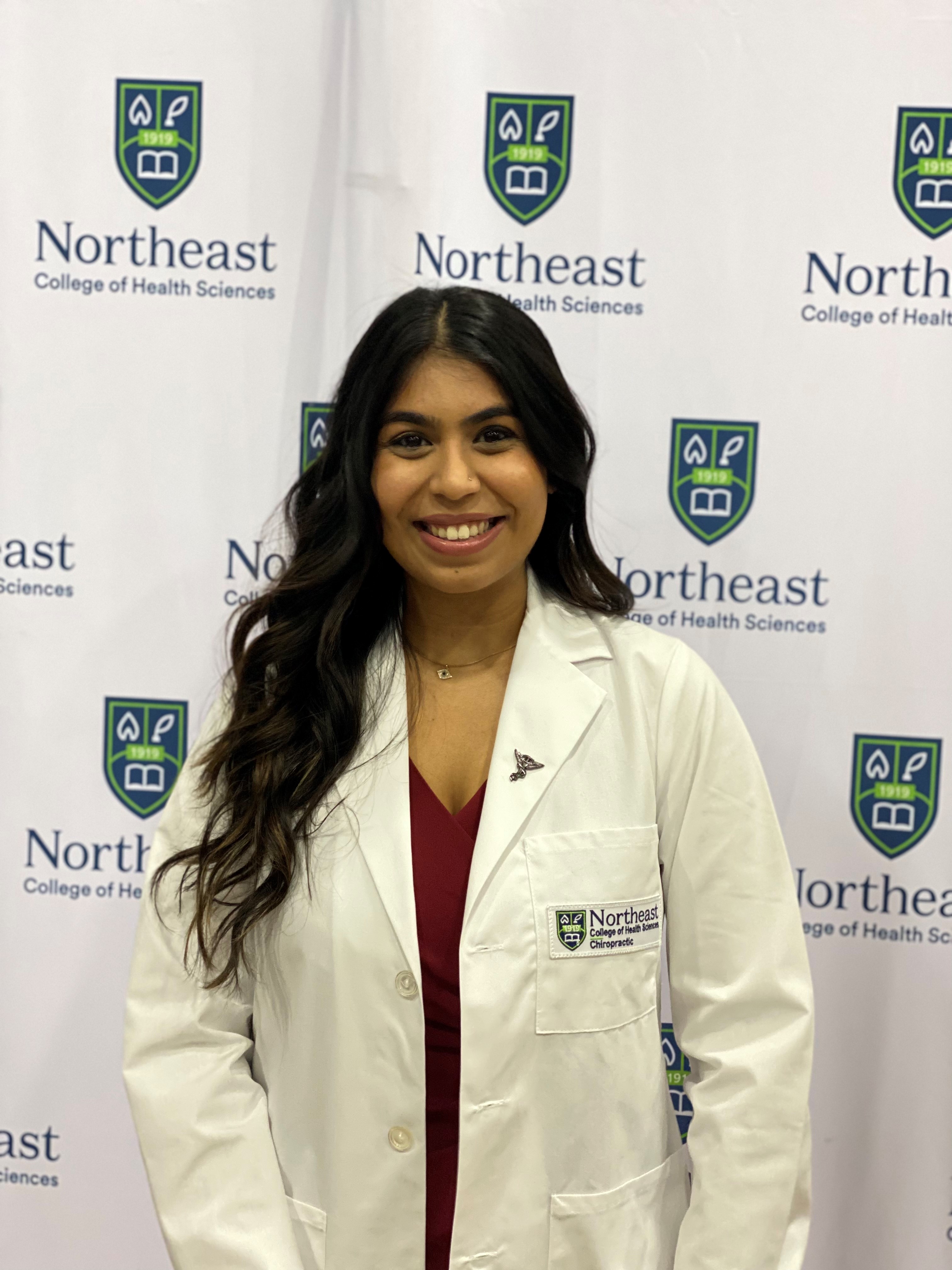 Jenna Patel smiles, wearing a clinical white coat